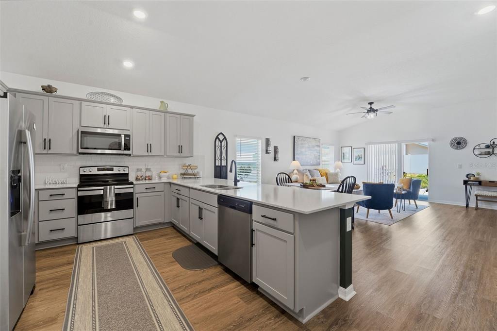 An open-concept living room and kitchen featuring a dark green accent wall and blue chairs — 15335 COPPER LOOP, BROOKSVILLE, FL