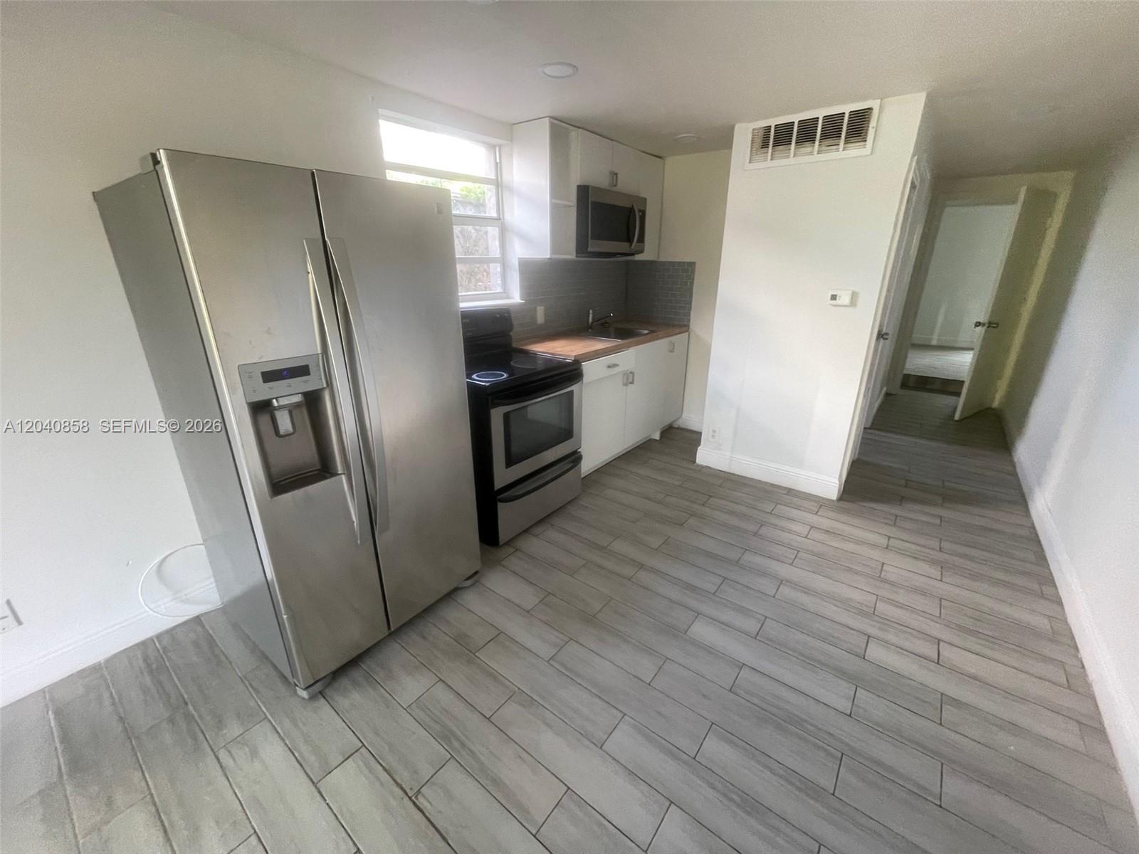 A kitchen features stainless steel appliances, white cabinetry, wood countertops, and gray tile flooring — 1865 NW 16th St # 1, Miami FL 33125, MIAMI, FL