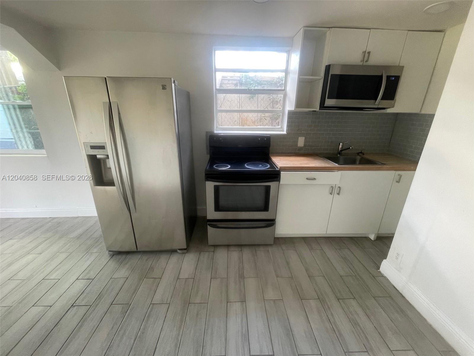 A kitchen features stainless steel appliances, white cabinets, a wood countertop, and gray tile flooring — 1865 NW 16th St # 1, Miami FL 33125, MIAMI, FL
