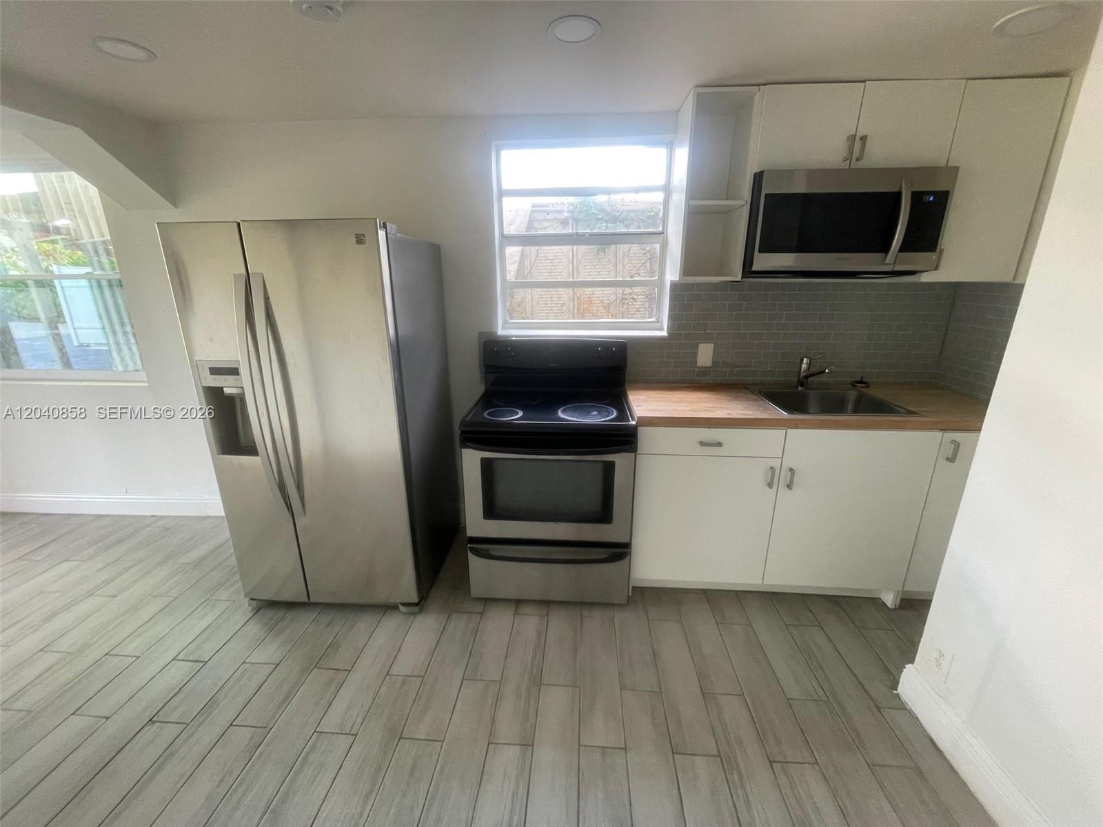 A kitchen features stainless steel appliances, white cabinets, a wood countertop, and gray tile flooring — 1865 NW 16th St # 1, Miami FL 33125, MIAMI, FL