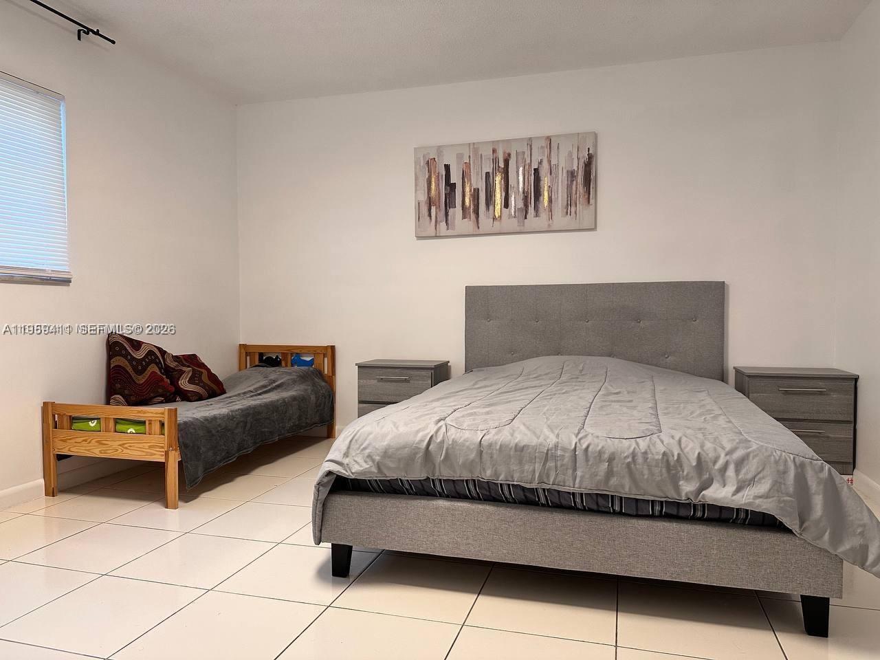 A bedroom features a gray upholstered bed, a wooden twin bed, and tile flooring — 319 NE 14th Ave # 106, Hallandale Beach FL 33009, HALLANDALE BEACH, FL