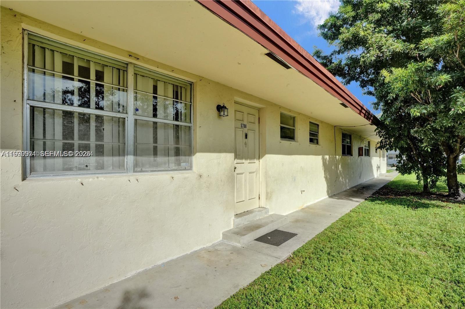 The exterior of a single-story building features a concrete walkway, a front door, and windows — 5706 Lincoln St, Hollywood FL 33021, HOLLYWOOD, FL