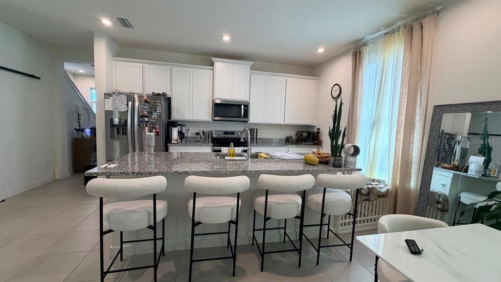 A kitchen features white cabinets, granite countertops, a central island with four stools, and tile flooring — 1978 EDUCATION STREET, ST CLOUD, FL