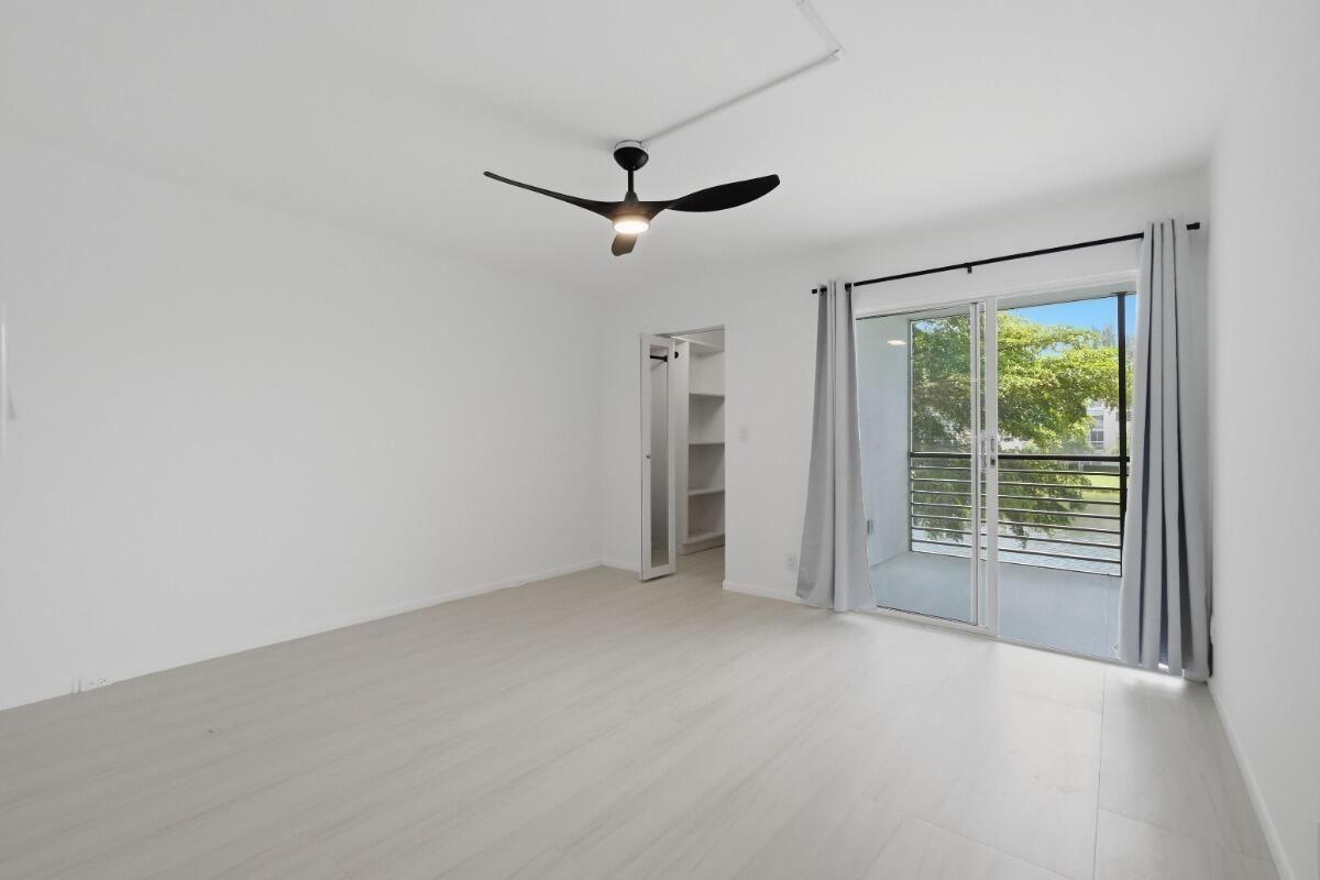 An empty bedroom features white walls, light wood-look flooring, a ceiling fan, and a balcony — 1805 Eleuthera Point # B2, Coconut Creek FL 33066, COCONUT CREEK, FL