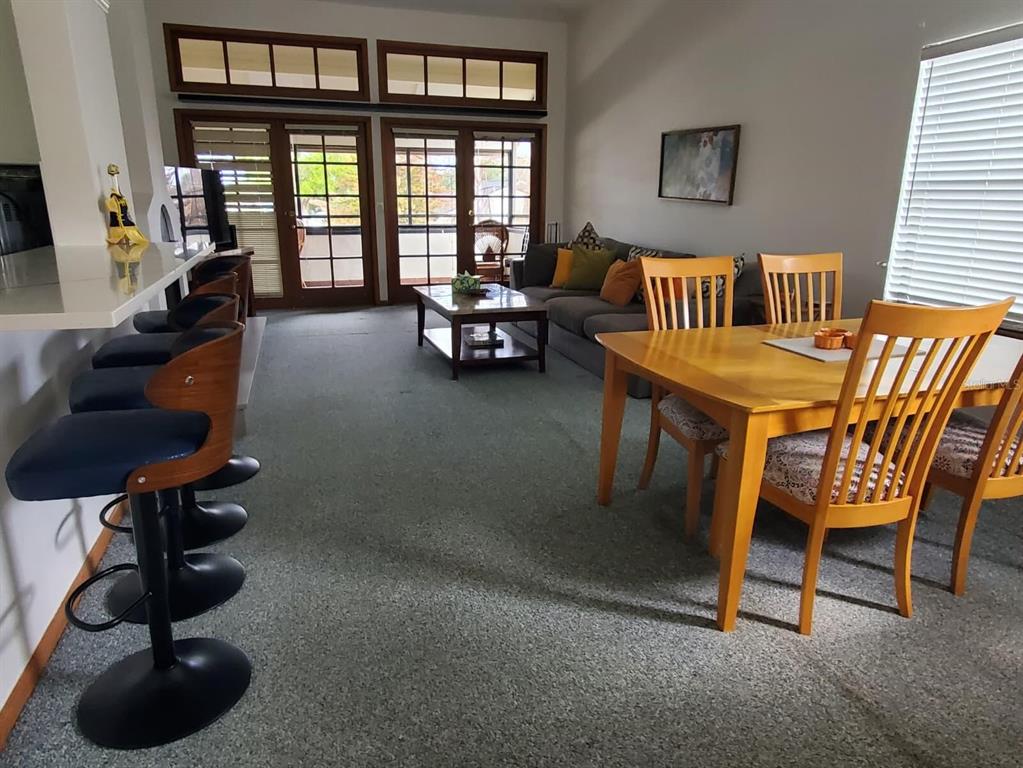 An open-concept living and dining area features carpeted floors, a breakfast bar, and glass doors — 2924 COTTAGE GROVE COURT UNIT GE, ORLANDO, FL