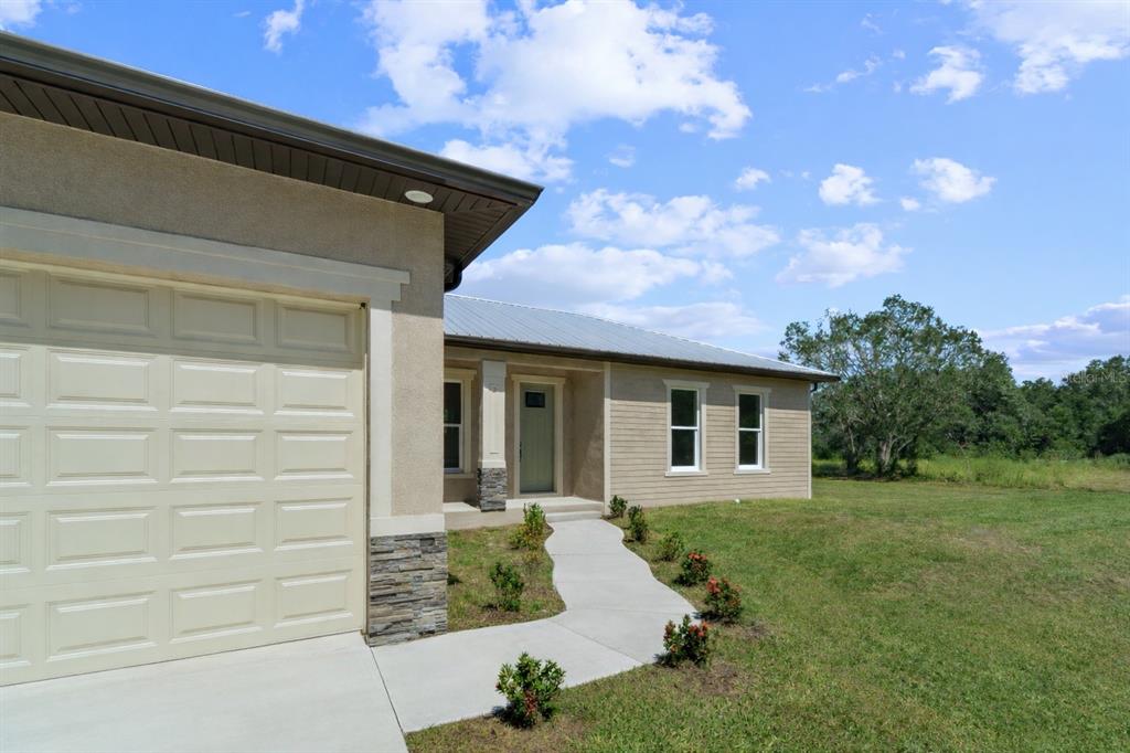 A tan stucco house with a metal roof, garage, and a concrete walkway leading to the entrance — 1201 NE CHILDRESS AVENUE, ARCADIA, FL