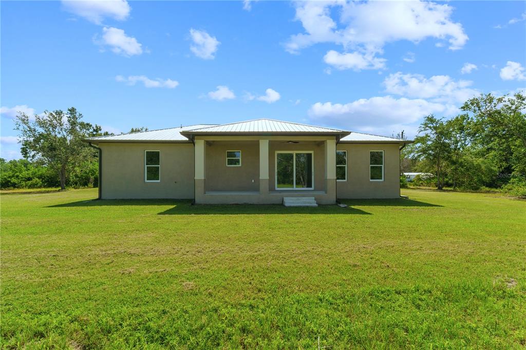 The exterior of a single-story house features a covered patio, a metal roof, and a large lawn — 1201 NE CHILDRESS AVENUE, ARCADIA, FL