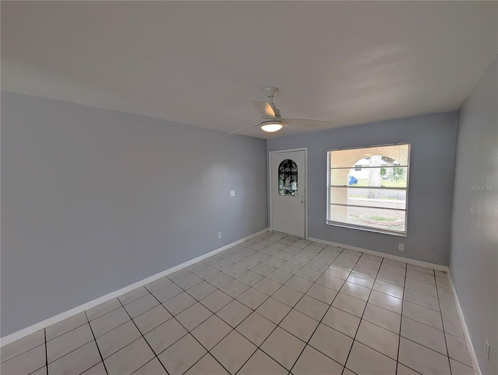 An empty room features light blue walls, white tile flooring, a ceiling fan, and a front door — 1803 E HUMPHREY STREET, TAMPA, FL