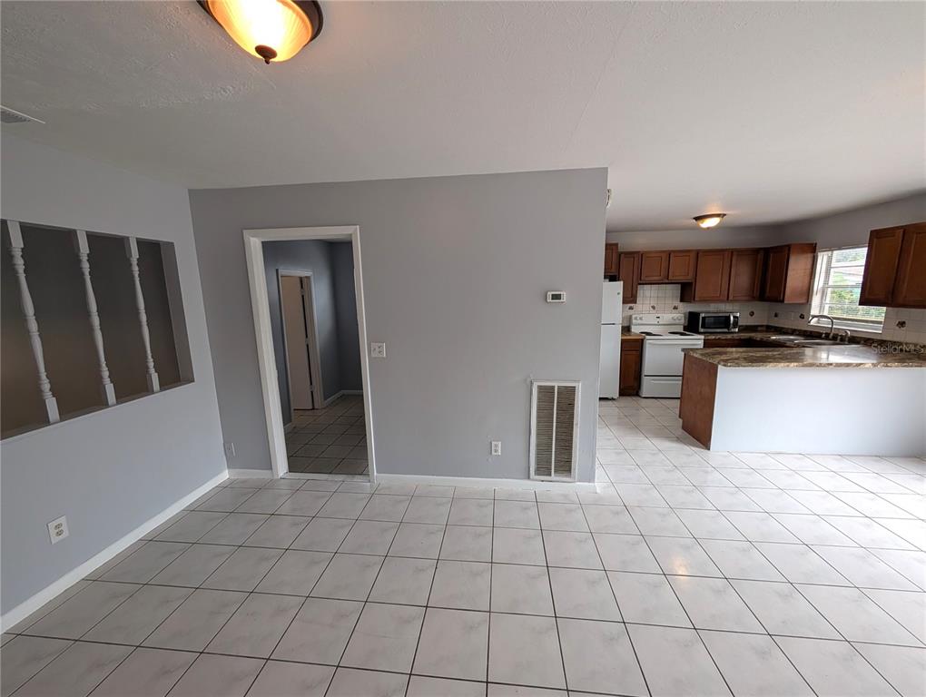 A room with light gray walls and white tile flooring leads into an open kitchen — 1803 E HUMPHREY STREET, TAMPA, FL