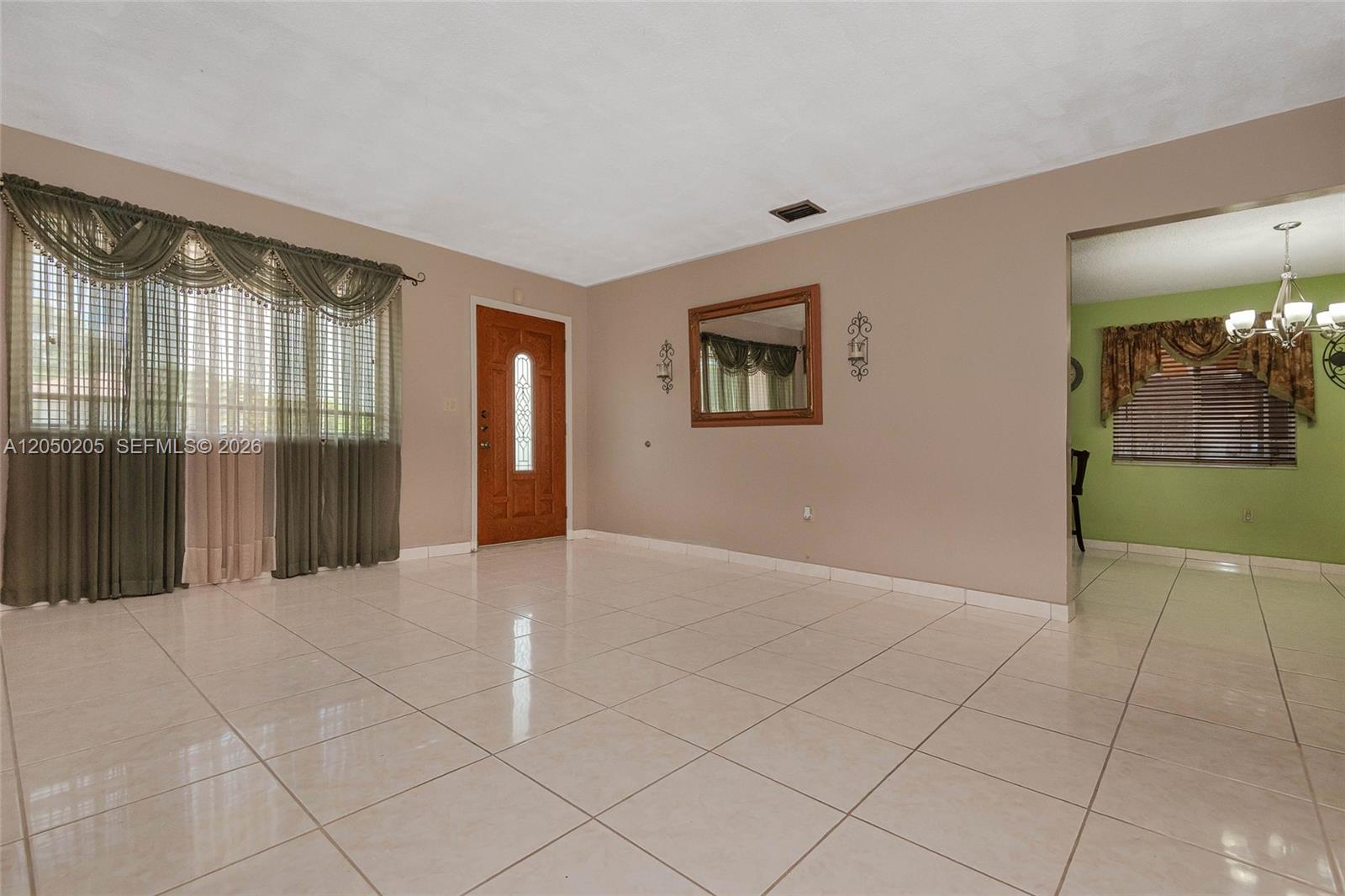 A living room features beige tile floors, tan walls, a wood front door, and curtains — 271 E 17th St, Hialeah FL 33010, HIALEAH, FL