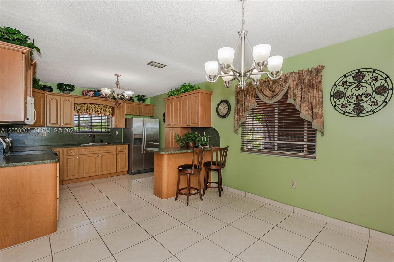 A kitchen features light wood cabinets, green walls, tile flooring, and a breakfast bar — 271 E 17th St, Hialeah FL 33010, HIALEAH, FL