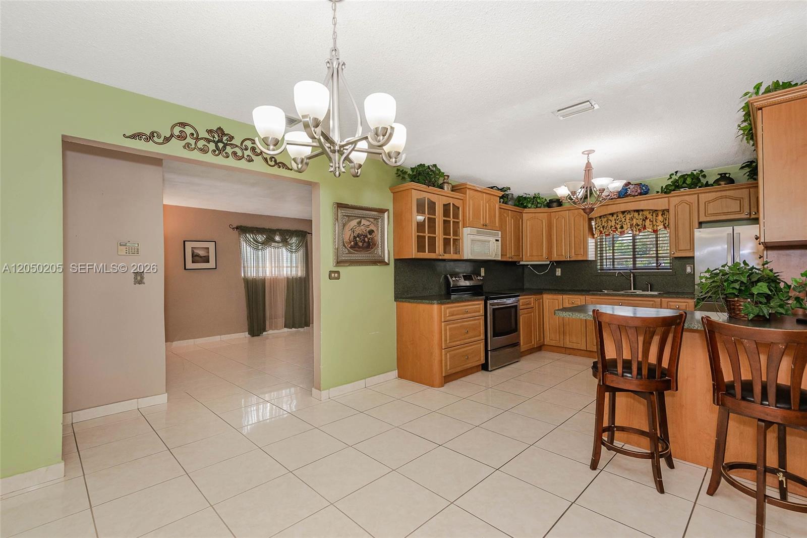 A kitchen with light wood cabinets and green walls opens into a dining area — 271 E 17th St, Hialeah FL 33010, HIALEAH, FL