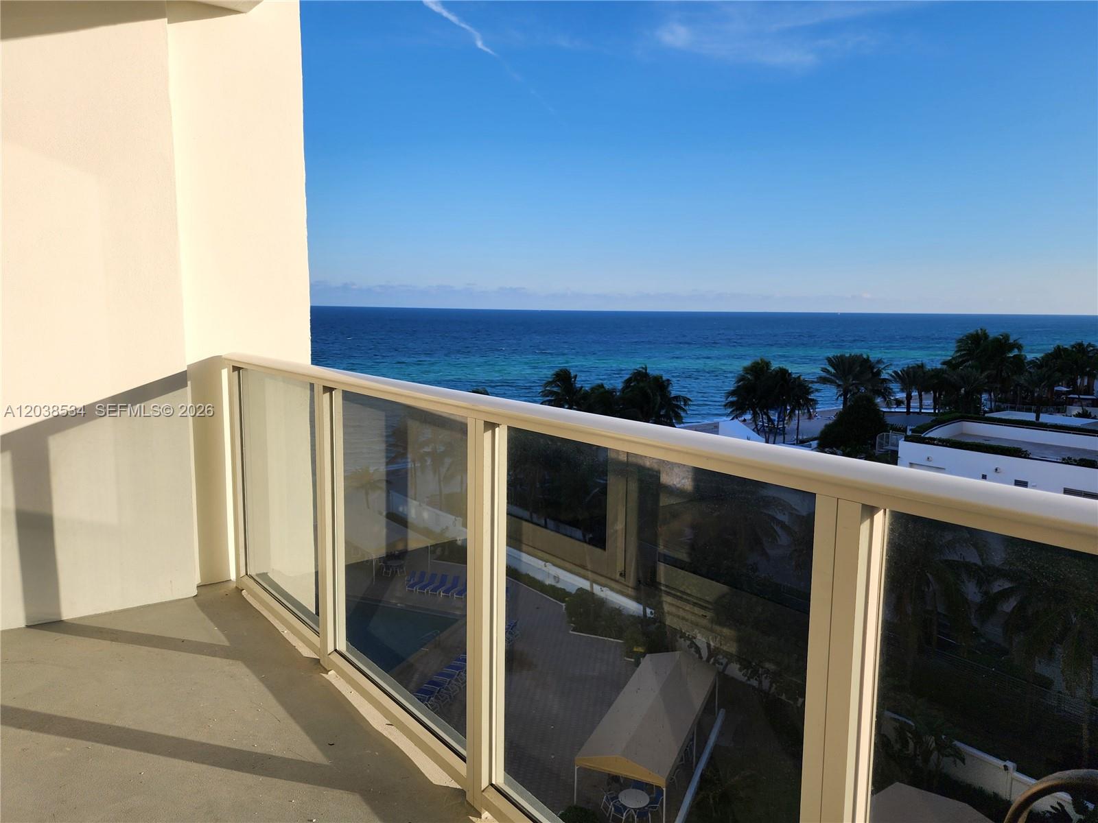A balcony with a glass railing overlooks the ocean and a pool area below — 3505 S Ocean Dr # 716, Hollywood FL 33019, HOLLYWOOD, FL