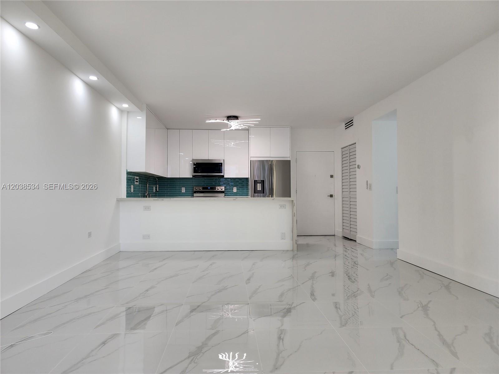 A modern kitchen features white cabinets, a teal backsplash, and white marble-patterned tile flooring — 3505 S Ocean Dr # 716, Hollywood FL 33019, HOLLYWOOD, FL