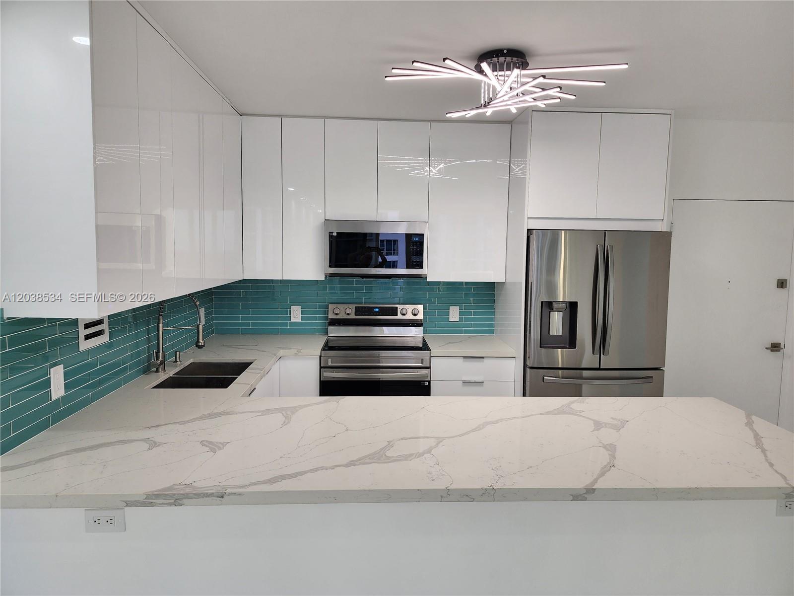 A modern kitchen features white glossy cabinets, a teal subway tile backsplash, and marble countertops — 3505 S Ocean Dr # 716, Hollywood FL 33019, HOLLYWOOD, FL