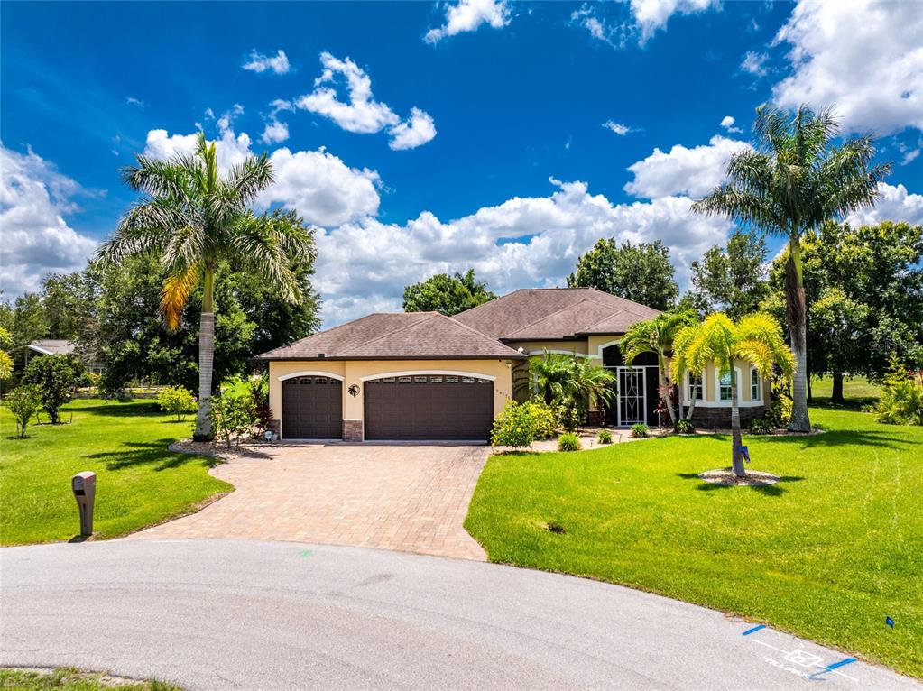 A single-story house with a three-car garage and palm trees sits on a grassy lot — 26171 MAMORA DRIVE, PUNTA GORDA, FL