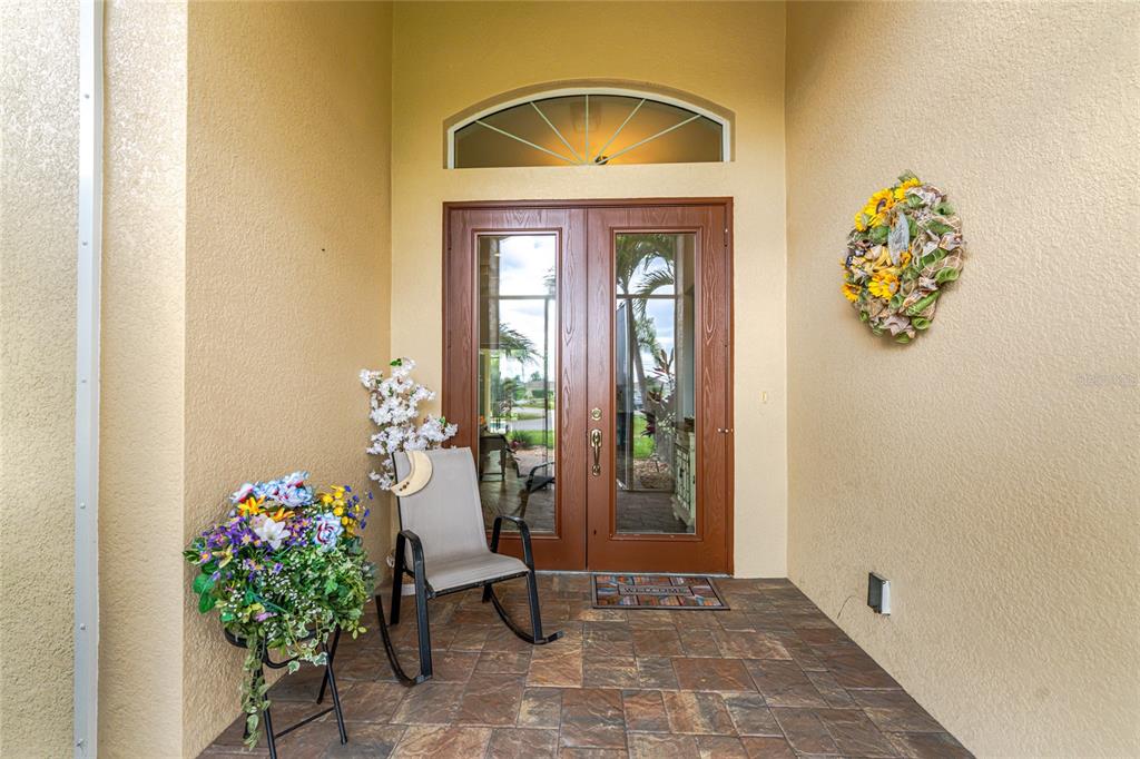 A covered entryway features double glass doors, a rocking chair, and a decorative floral wreath — 26171 MAMORA DRIVE, PUNTA GORDA, FL