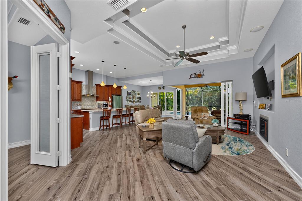An open-concept living room and kitchen feature wood-look flooring, a tray ceiling, and sliding doors — 26171 MAMORA DRIVE, PUNTA GORDA, FL