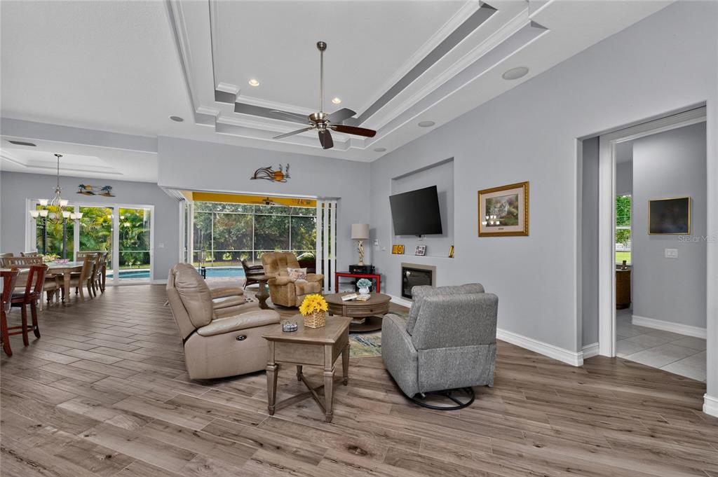 A living room with wood-look tile flooring, a tray ceiling, and sliding doors to a pool — 26171 MAMORA DRIVE, PUNTA GORDA, FL