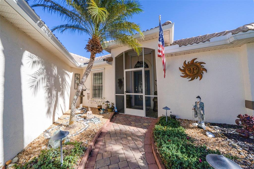 A paved walkway leads to a screened front entryway of a house with a palm tree — 4115 CAPE COLE BOULEVARD, PUNTA GORDA, FL