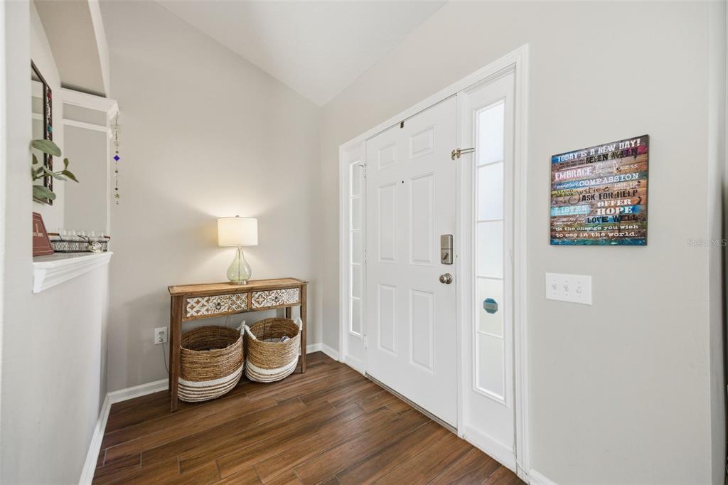 An entryway features a white front door, wood-look flooring, and a console table with baskets — 25114 LEXINGTON OAKS BOULEVARD, WESLEY CHAPEL, FL