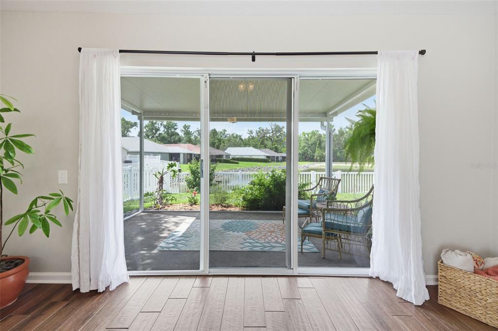 A room with wood-look flooring features sliding glass doors opening to a covered patio — 25114 LEXINGTON OAKS BOULEVARD, WESLEY CHAPEL, FL