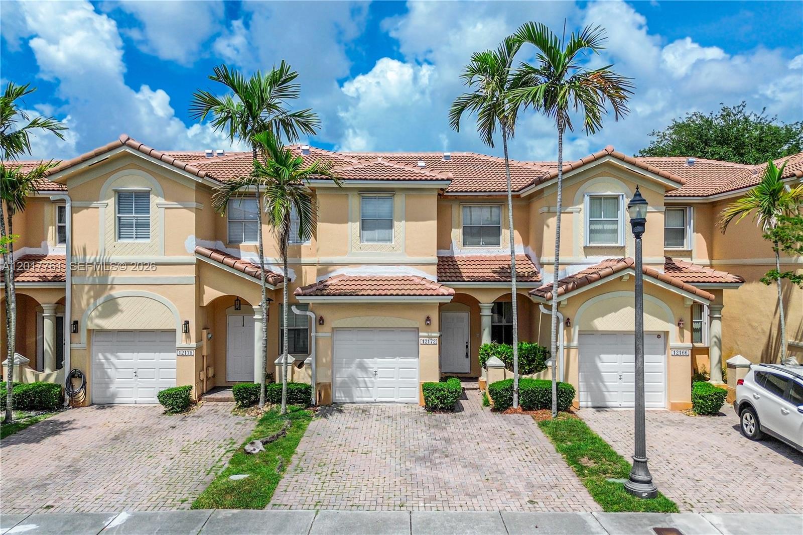 A row of three two-story townhouses with beige stucco walls, tiled roofs, and attached garages — 12172 SW 124th Path, Miami FL 33186, MIAMI, FL