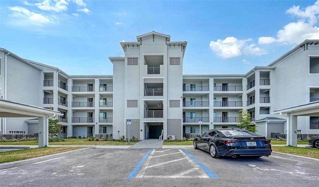 A multi-story apartment building exterior features balconies and a parking lot with a parked car — 17600 OPAL SAND DRIVE UNIT 301, VENICE, FL