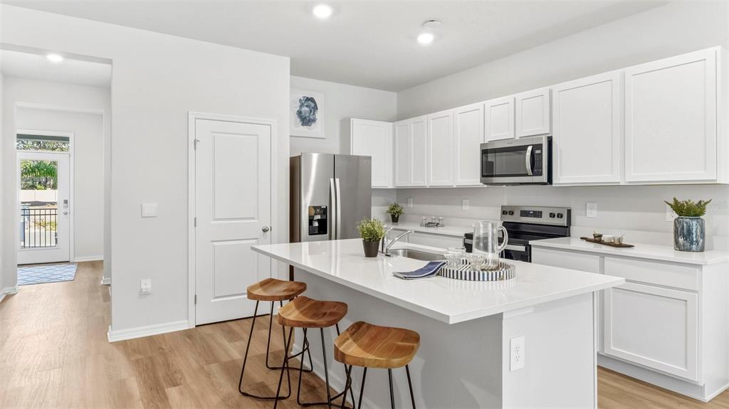 A modern kitchen features white cabinets, a quartz island with three stools, and stainless appliances — 4040 GOLD DUST LANE, SARASOTA, FL