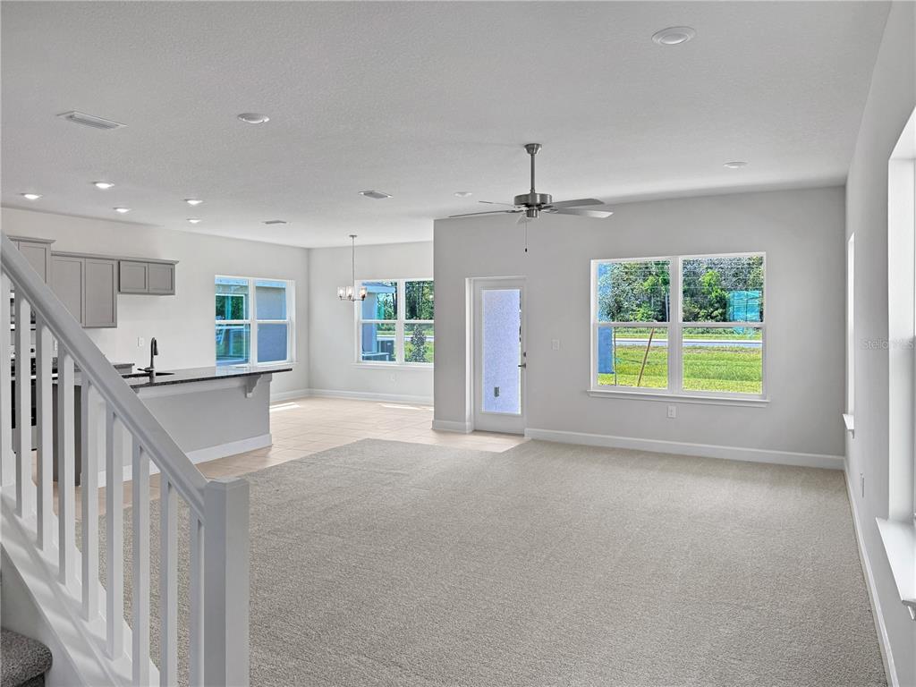 An open-concept living area features a carpeted floor, a kitchen with gray cabinets, and a ceiling fan — 4026 SAGEFIELD DRIVE, ST CLOUD, FL