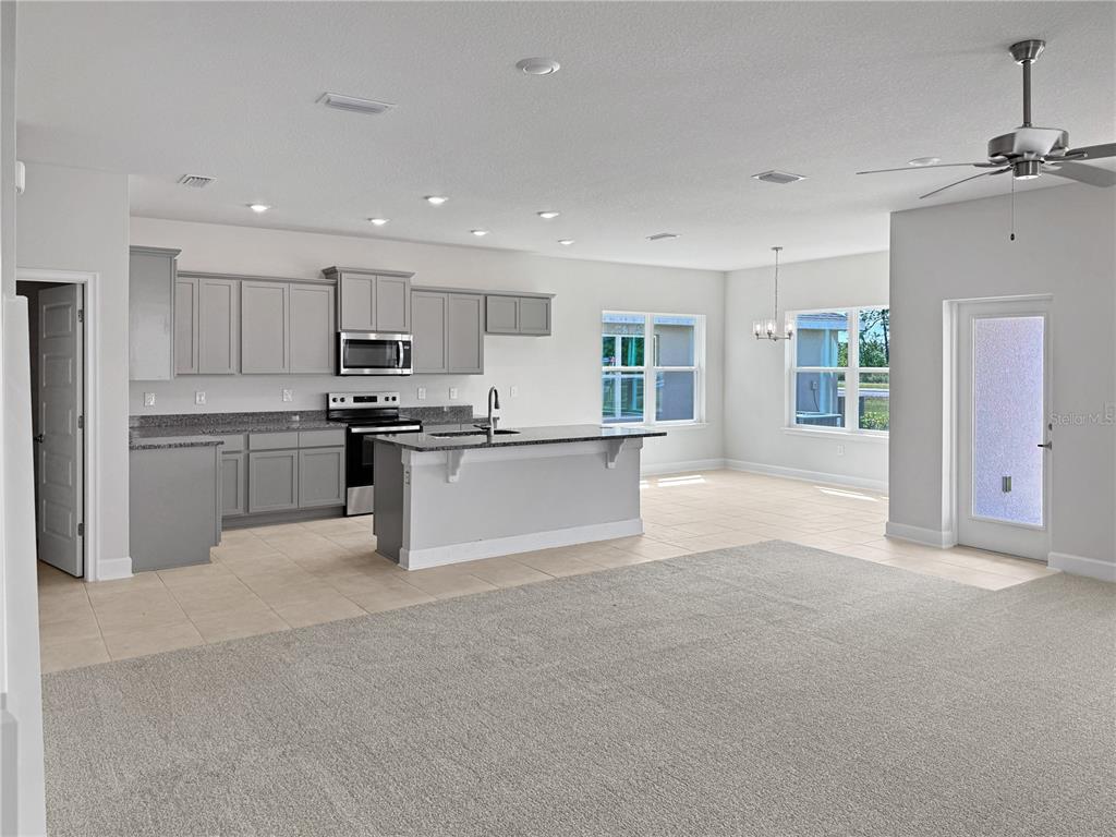 An open-concept kitchen features gray cabinetry, granite countertops, and tile flooring adjacent to carpeted space — 4026 SAGEFIELD DRIVE, ST CLOUD, FL