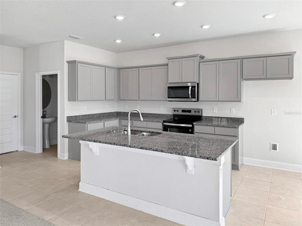 A kitchen features gray cabinets, granite countertops, a central island, and stainless steel appliances — 4026 SAGEFIELD DRIVE, ST CLOUD, FL
