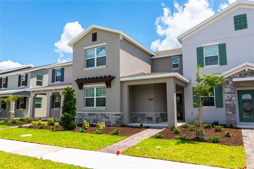 The exterior of a two-story townhouse features a stone-accented facade, a covered entryway, and landscaping — 11763 BOLDFACE DRIVE, ORLANDO, FL