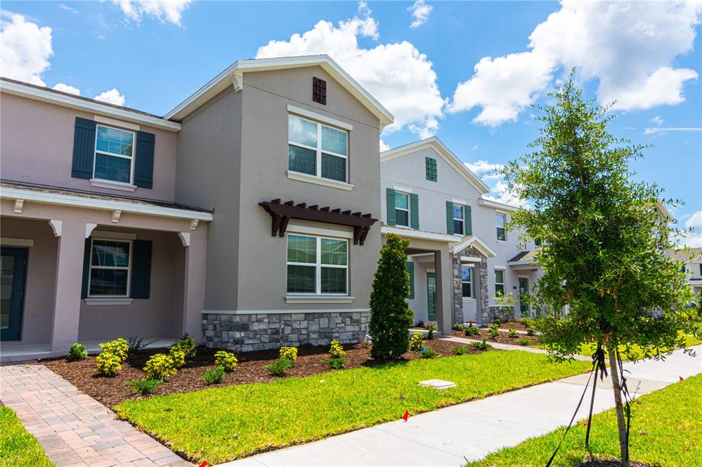 A two-story townhouse exterior features tan stucco walls, stone accents, and a paved walkway — 11763 BOLDFACE DRIVE, ORLANDO, FL