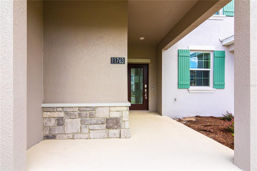 A covered entryway features a stone-accented wall, a dark wood front door, and a window with green shutters — 11763 BOLDFACE DRIVE, ORLANDO, FL