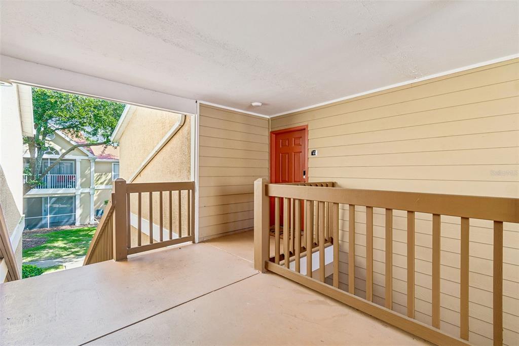 An outdoor apartment landing features a tan floor, beige siding, and a red front door — 9481 HIGHLAND OAK DRIVE UNIT 814, TAMPA, FL