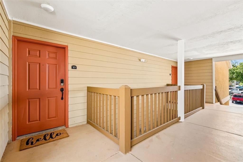 An exterior view of an apartment entrance with an orange door and a wooden railing — 9481 HIGHLAND OAK DRIVE UNIT 814, TAMPA, FL