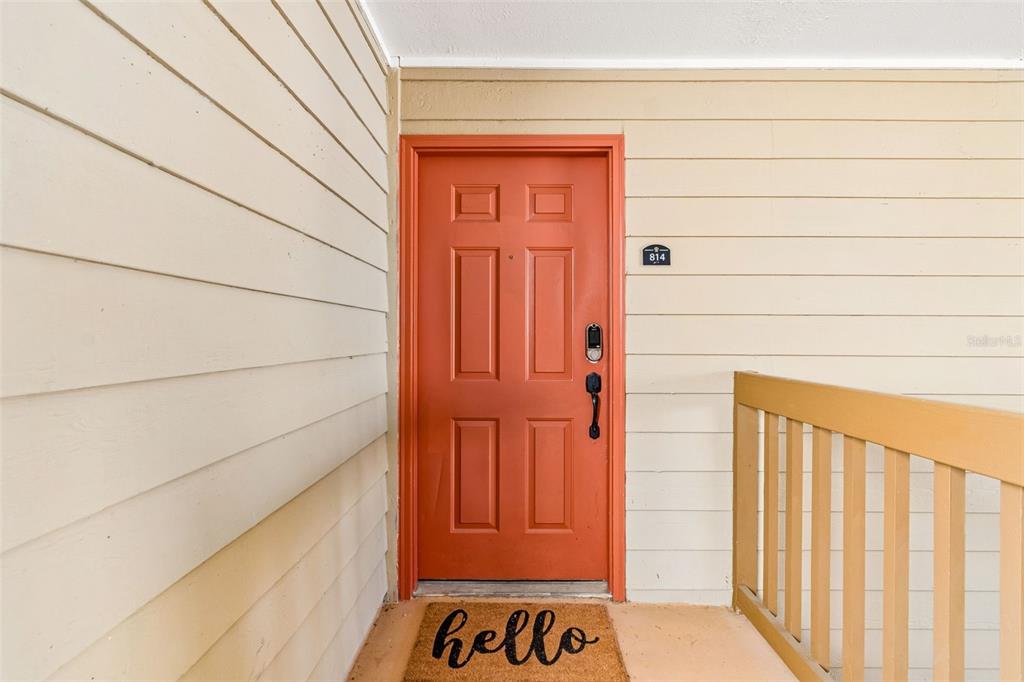 An orange front door with a welcome mat sits on a covered apartment balcony — 9481 HIGHLAND OAK DRIVE UNIT 814, TAMPA, FL