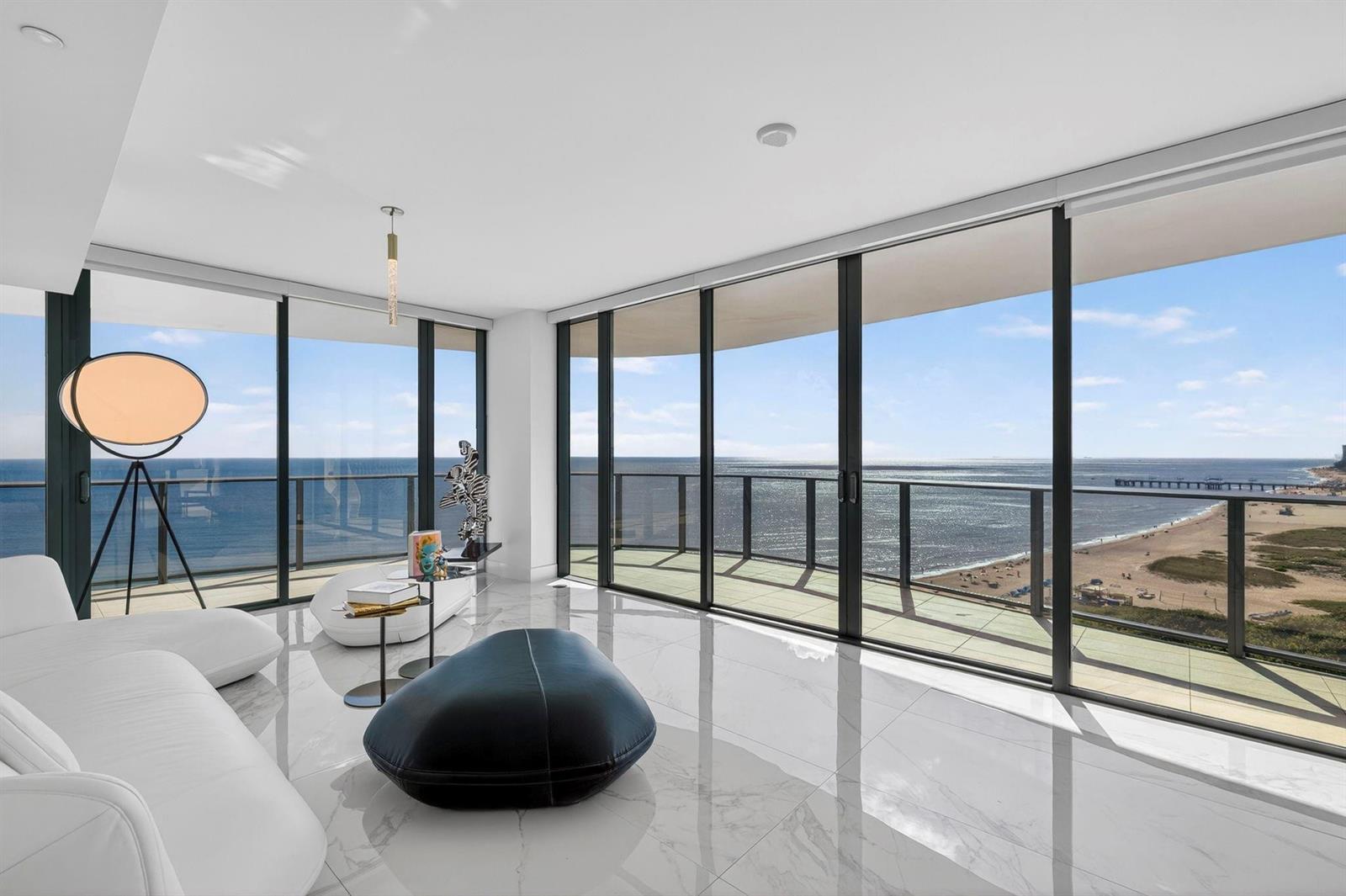 A modern living room with white marble floors, floor-to-ceiling windows, and a balcony overlooking the ocean — 730 N Ocean Boulevard # 1204, Pompano Beach FL 33062, POMPANO BEACH, FL