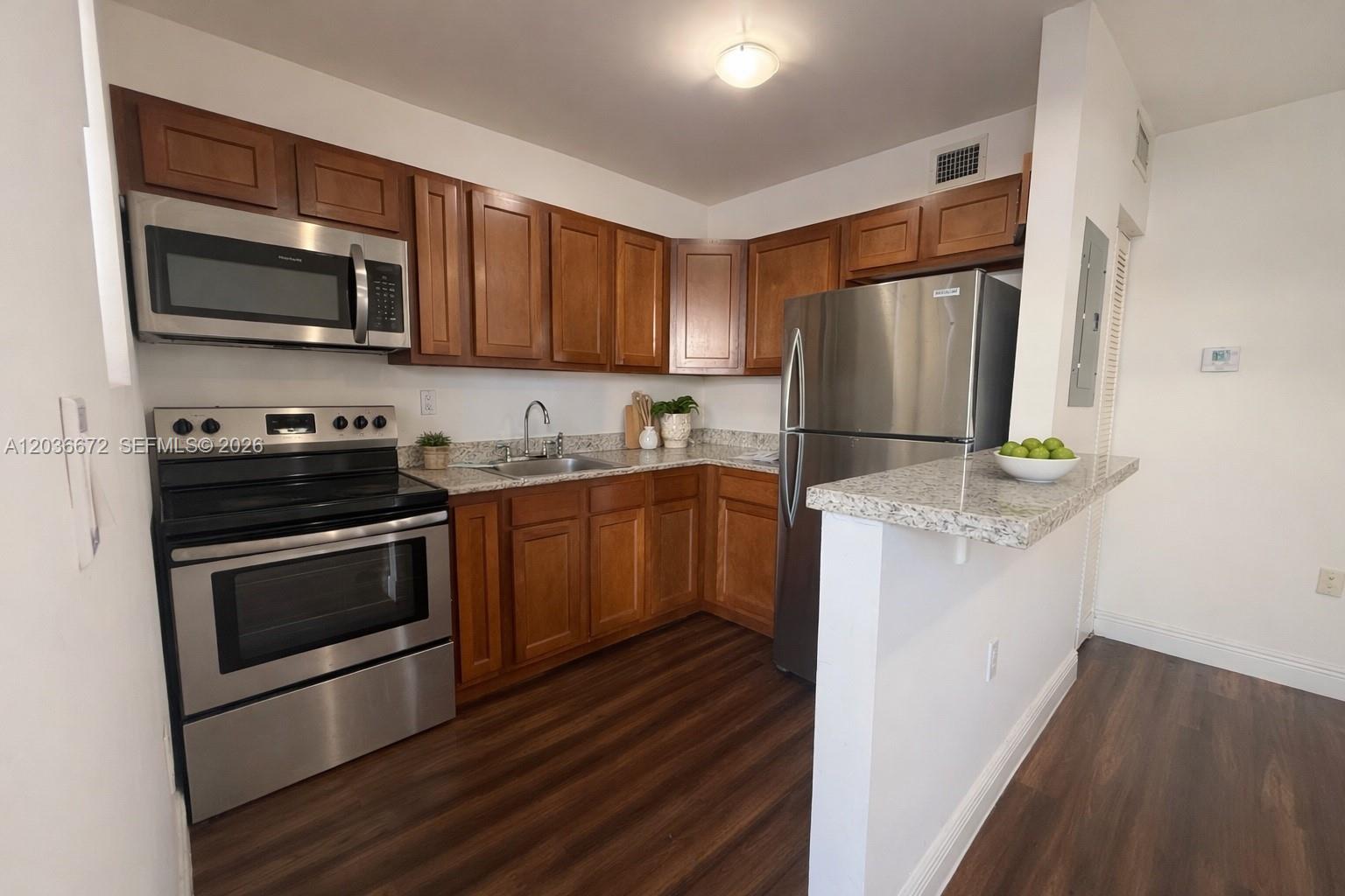 A kitchen features wood cabinets, stainless steel appliances, and granite countertops over dark wood flooring — 540 NW 7th St # 4, Miami FL 33136, MIAMI, FL