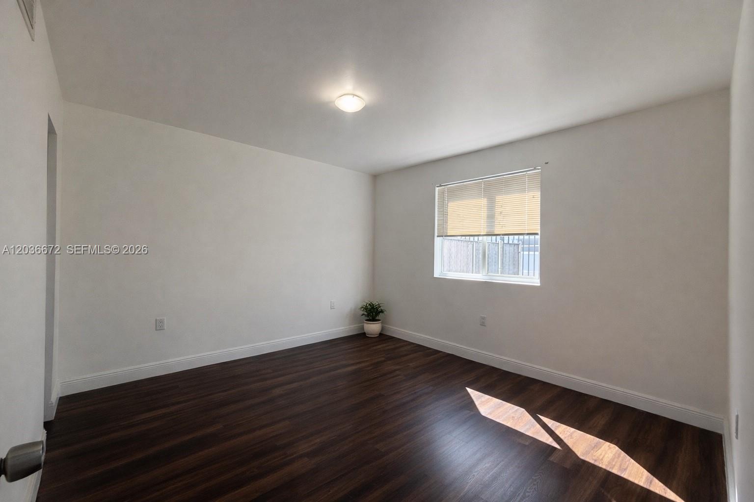 An empty bedroom features white walls, dark wood-look flooring, a window with blinds, and a ceiling light — 540 NW 7th St # 4, Miami FL 33136, MIAMI, FL
