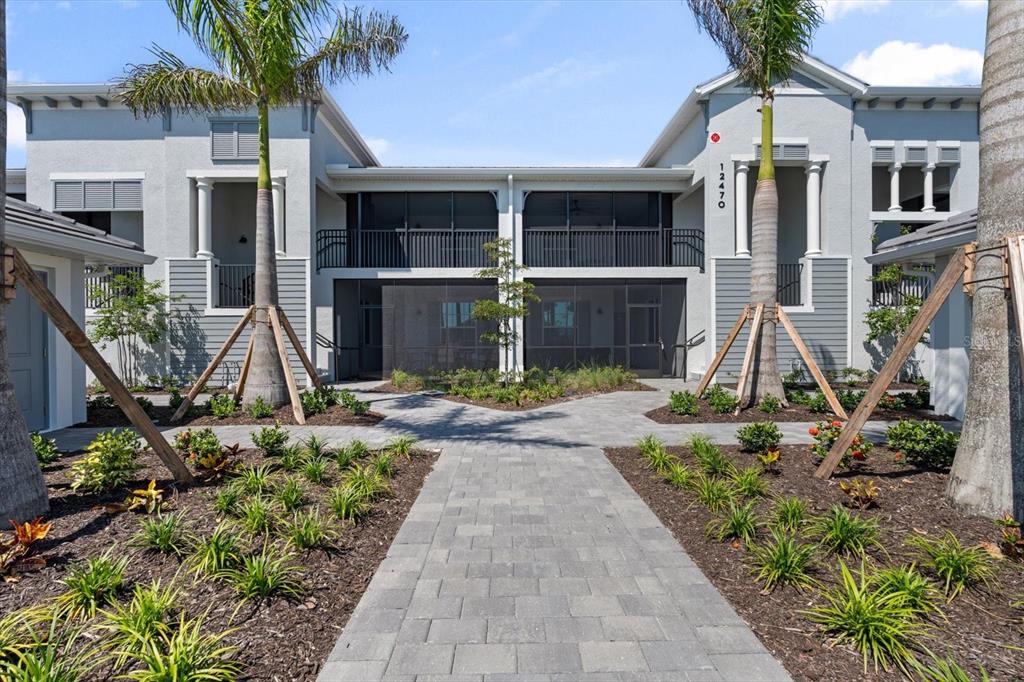 A paved walkway leads to the entrance of a two-story building with screened balconies — 12470 WELLEN GOLF STREET UNIT 205, VENICE, FL