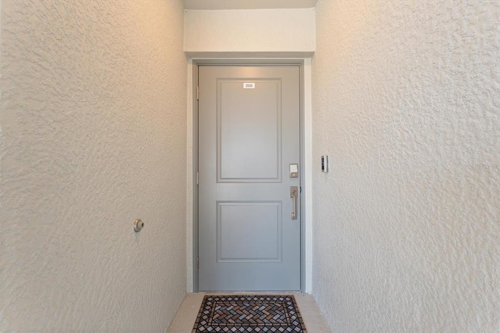 A gray front door with the number 205 is set into a textured white wall — 12470 WELLEN GOLF STREET UNIT 205, VENICE, FL