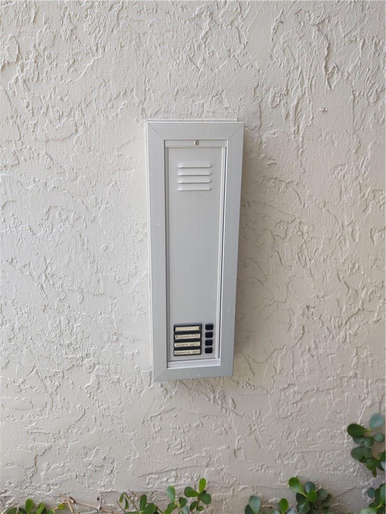A white intercom system with four buttons is mounted on a textured exterior stucco wall — 5801 Coach House Circle # B, Boca Raton FL 33486, BOCA RATON, FL