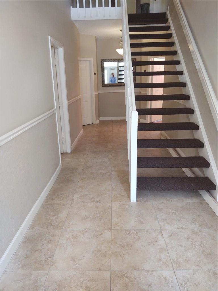 A foyer with beige tile flooring features a staircase with brown carpeted steps — 5801 Coach House Circle # B, Boca Raton FL 33486, BOCA RATON, FL