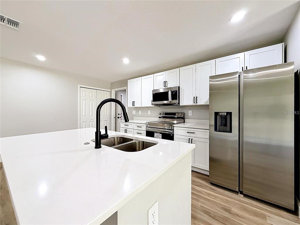 A modern kitchen features white cabinets, stainless steel appliances, and a large white island — 44 DOGWOOD DRIVE COURSE, OCALA, FL
