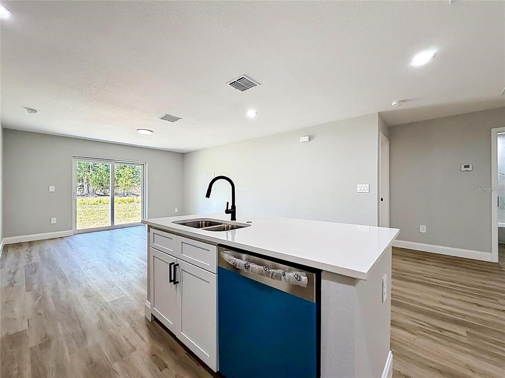 A kitchen island with a sink and dishwasher faces an open living area with sliding doors — 44 DOGWOOD DRIVE COURSE, OCALA, FL