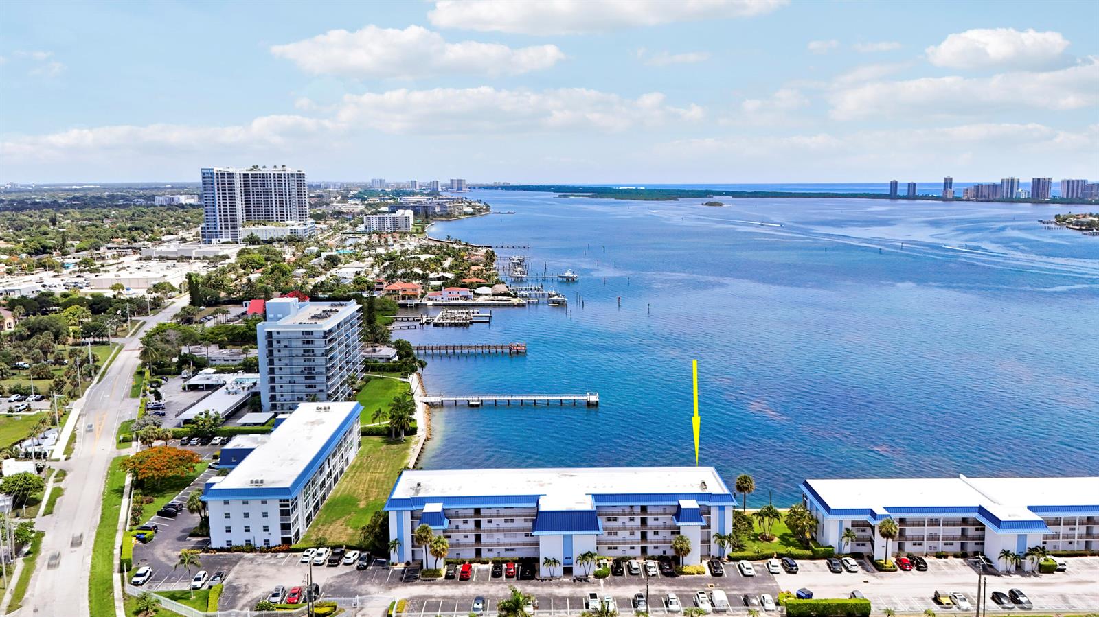 An aerial view shows a multi-story apartment building situated along a waterfront with a pier — 410 Wilma Circle # 308, Riviera Beach FL 33404, RIVIERA BEACH, FL