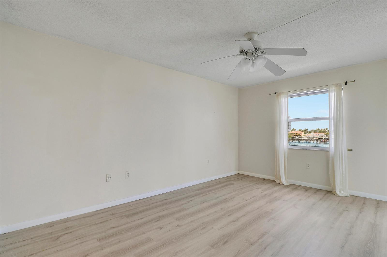 An empty bedroom features light wood-look flooring, a ceiling fan, and a window with curtains — 410 Wilma Circle # 308, Riviera Beach FL 33404, RIVIERA BEACH, FL