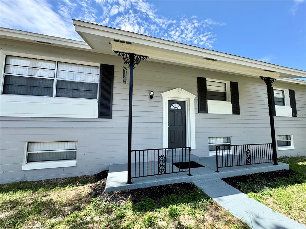 A gray house exterior features a front door, black railings, and decorative metal porch supports — 6802 NAWADAHA BOULEVARD, ORLANDO, FL